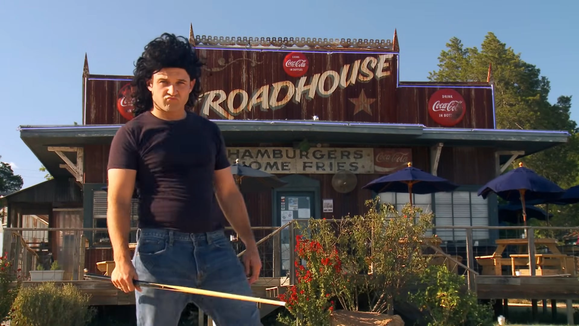 A man standing in front of the Roadhouse restaurant in Bastrop, Texas, holding a wooden stick, with the building's vintage signage in the background